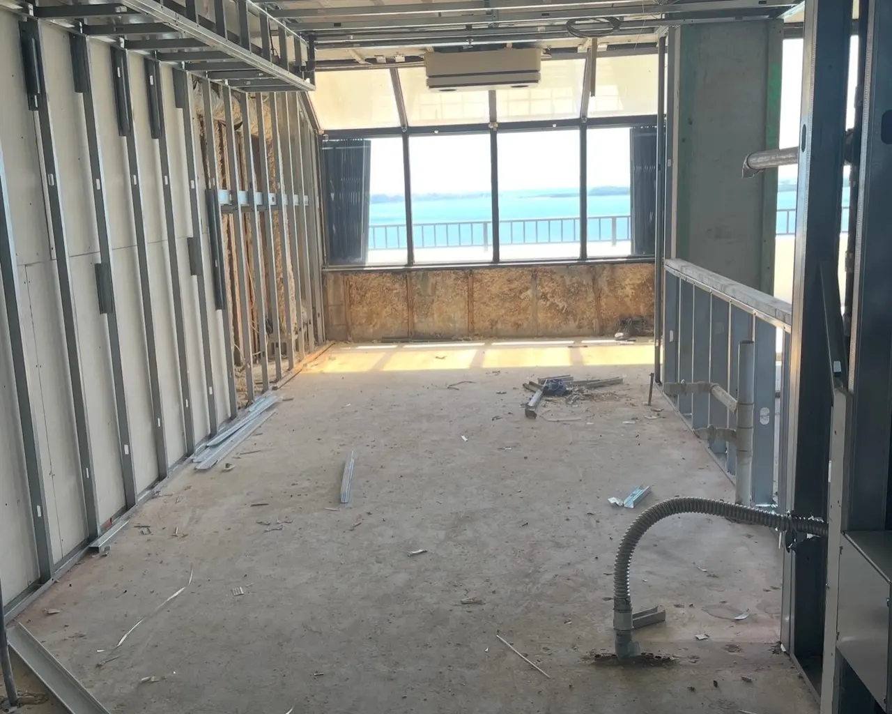 The apartment stripped to metal studs and bare concrete, with the bay behind the openings